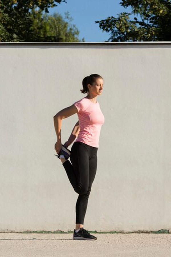 A woman stretching her leg during an outdoor workout, wearing athletic clothing.