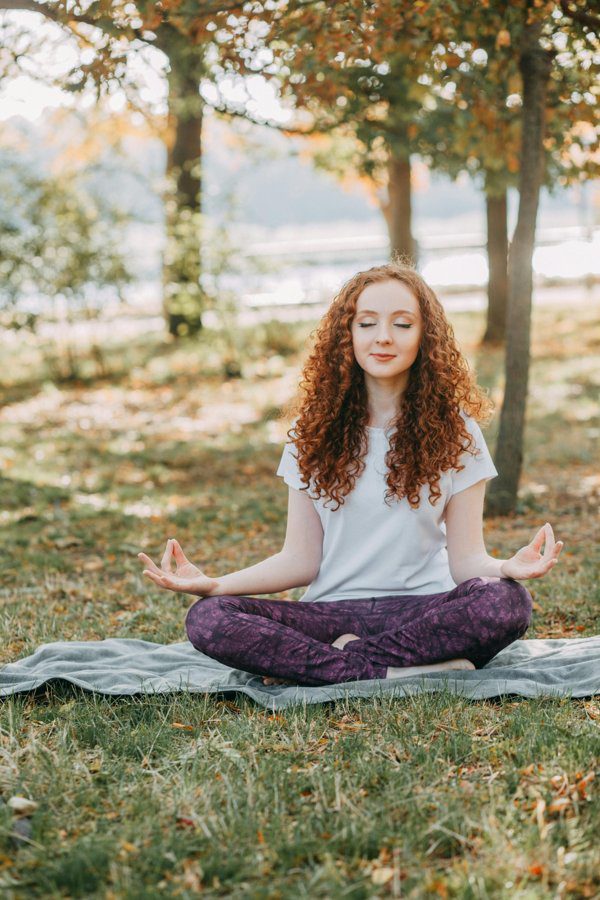 A woman practicing mindfulness meditation outdoors, sitting on a mat with a peaceful expression, embodying mental wellness and tranquility.